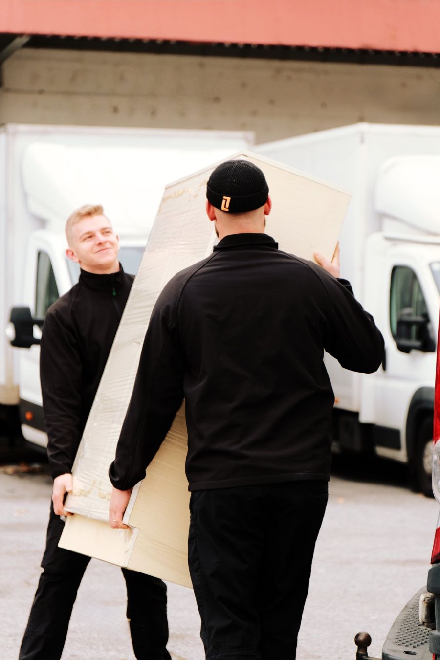 Zwei packdas!-Möbelpacker tragen einen in Folie verpackten Kasten zum Transporter – Entrümpelung 1010 Wien (Innere Stadt)