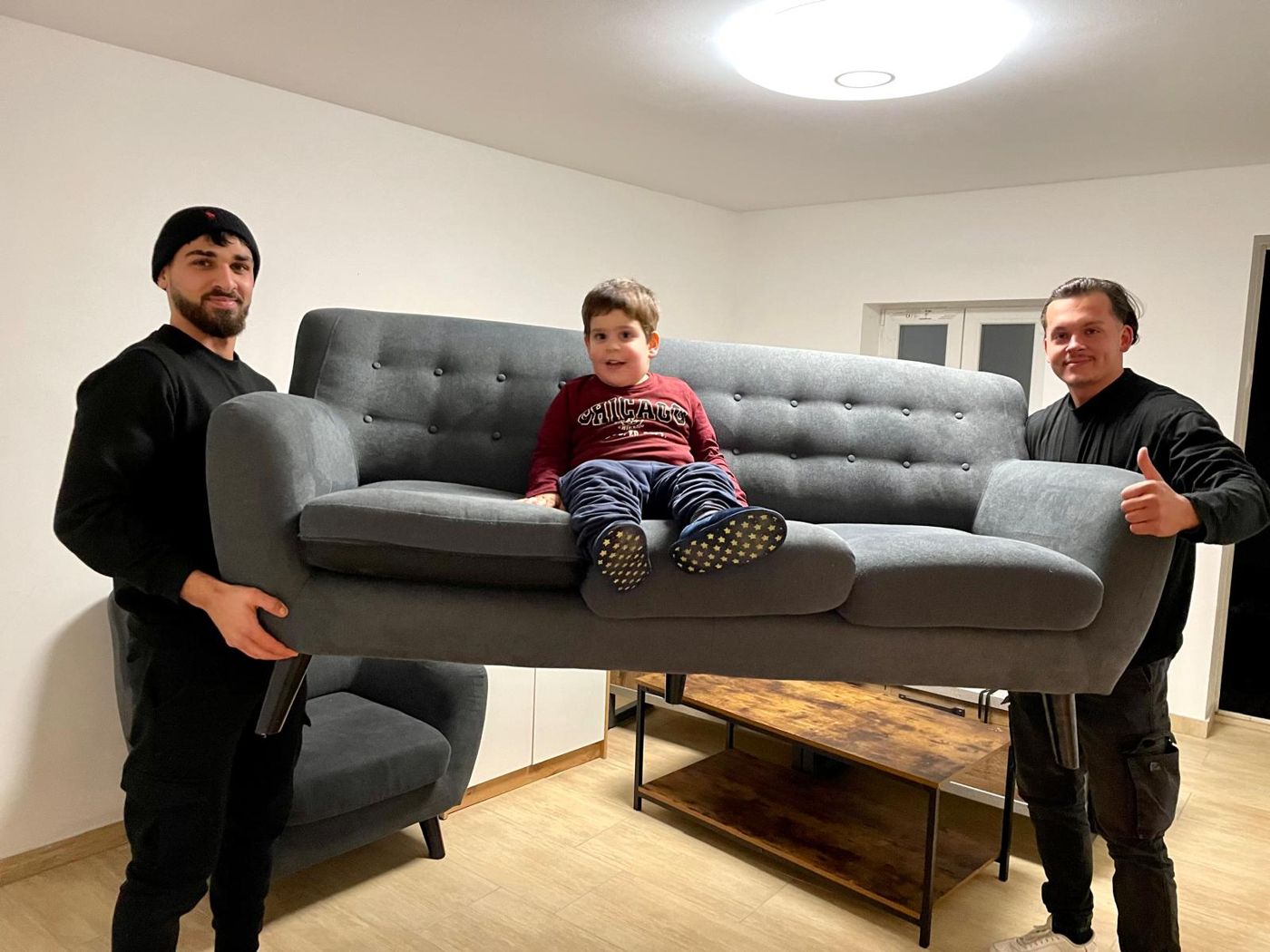 Zwei packdas!-Möbelpacker tragen ein graues Sofa durch eine Wohnung – Firmenumzug Wien